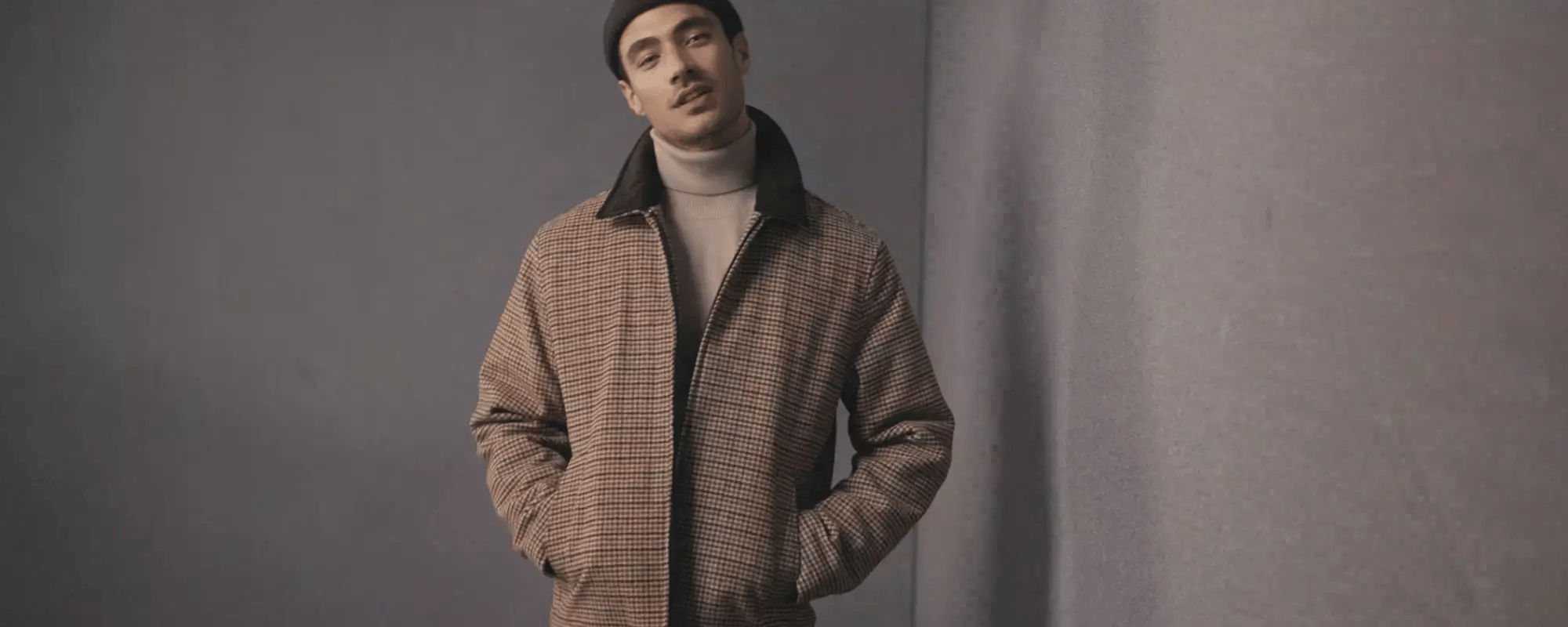 Man wearing a checkered jacket over a turtleneck sweater against a plain background