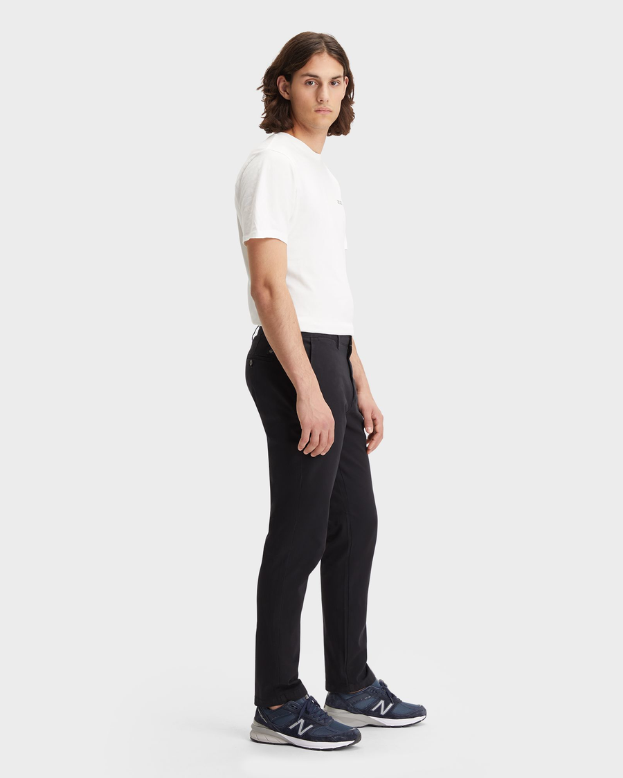 Side view of model wearing Black Men's Slim Fit Smart 360 Flex Alpha Chino Pants.