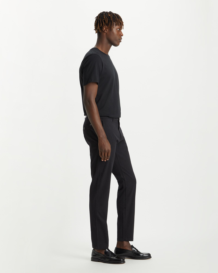 Side view of model wearing Black Men's Slim Tapered Fit Smart 360 Flex Alpha Chino Pants.