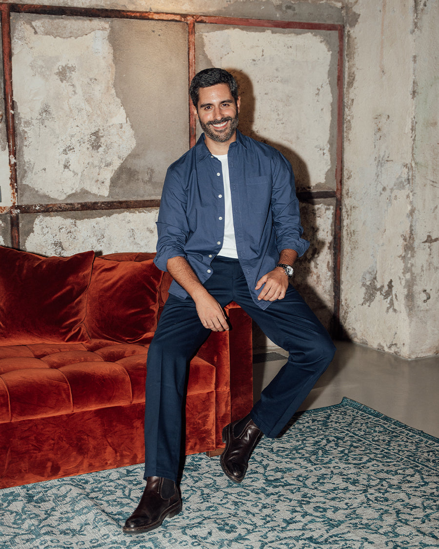 Man sitting on a red velvet couch in a room with textured walls and a patterned rug.