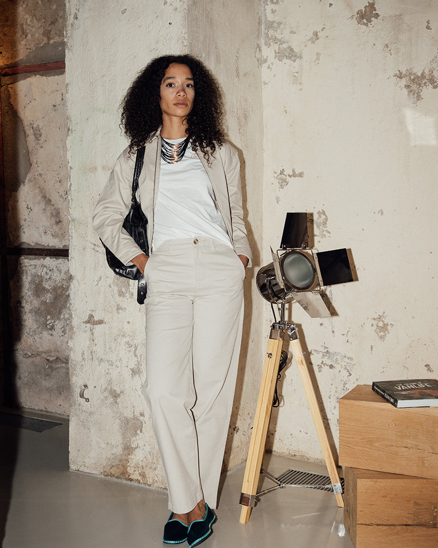Woman standing next to a vintage-style camera on a wooden stand against a textured wall.