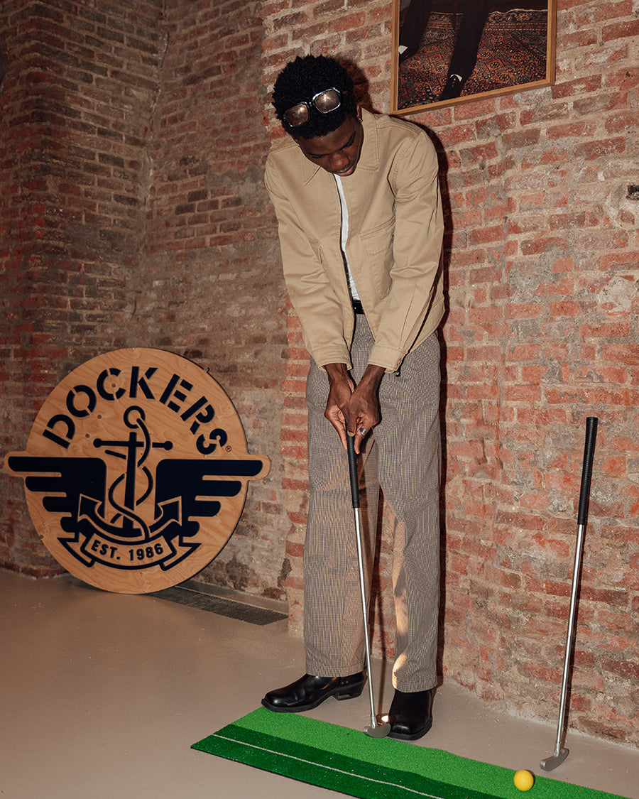 Man playing mini golf in front of a brick wall with a Dockers logo.